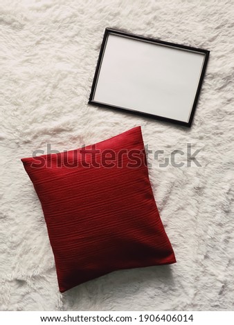Black thin wooden frame with blank copyspace as poster photo print mockup, red cushion pillow and fluffy white blanket, flat lay background and art product, top view