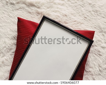 Black thin wooden frame with blank copyspace as poster photo print mockup, red cushion pillow and fluffy white blanket, flat lay background and art product, top view