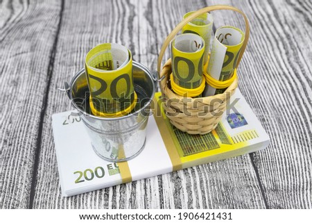 Rolled 200 euro banknotes stand in a small bucket and basket on a bundle of banknotes. High quality photo