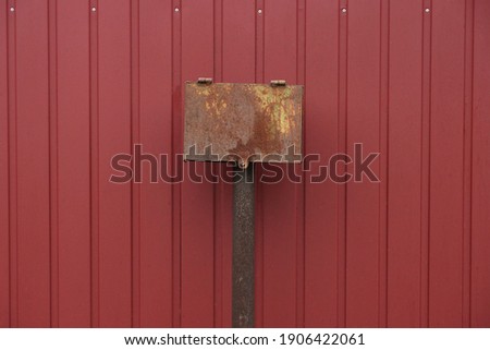 one brown rusty iron box for electrical wires by a red metal fence wall outside