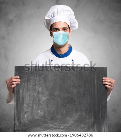 Masked chef or cook holding a blackboard during covid coronavirus pandemic, restaurants and food concept