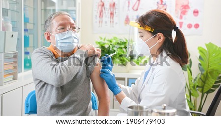 asian female doctor wearing gloves and isolation mask is making a vaccination in the shoulder of senior male patient at hospital Royalty-Free Stock Photo #1906479403