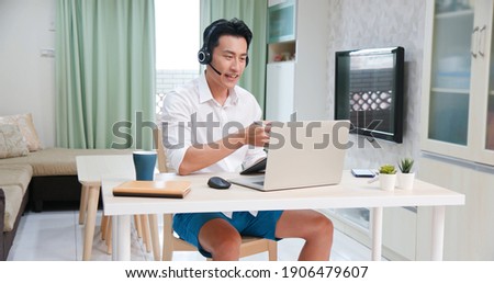 telework concept - Asian man wear headset use laptop to join a video meeting at home freely Royalty-Free Stock Photo #1906479607
