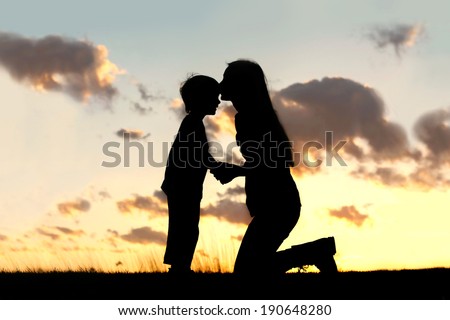 Silhouette of a young mother lovingly kissing her little child on the forehead, outside isolated in front of a sunset in the sky on a summer day. Royalty-Free Stock Photo #190648280