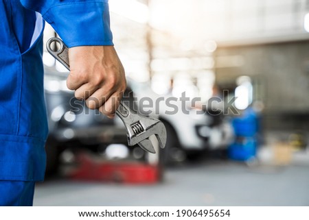 Mechanic close up fixing repairing car engine automobile vehicle parts examining screwing using tools wrench equipment working hard in workshop garage support and service in overall work uniform Royalty-Free Stock Photo #1906495654