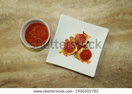 Top view of no crust keto pizza bites on a white square plate and marinara dipping sauce on the side for appetizer.