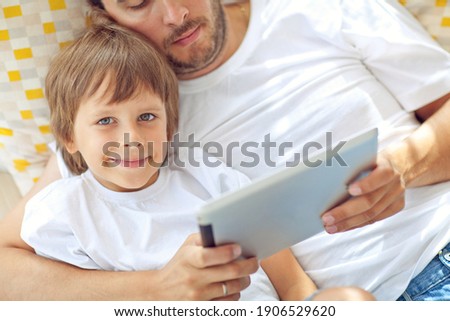 Son and father are playing a computer game on a tablet. . High quality photo