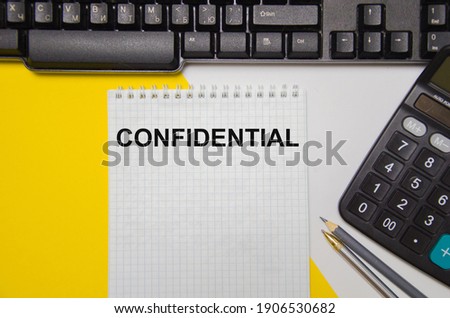 the word confidential written on a yellow and white background near a computer keyboard and calculator. High quality photo