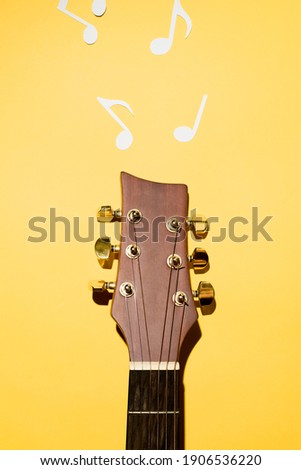 Acoustic guitar neck and sheet music cut from paper. Yellow background, flat lay.