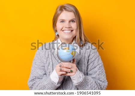 A nice picture of a woman holding a globe with both hands and smiling is looking at the camera .