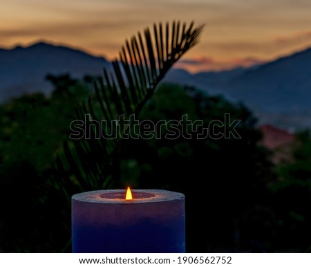 Decorative burning candle on blurred background with sunrise above mountains