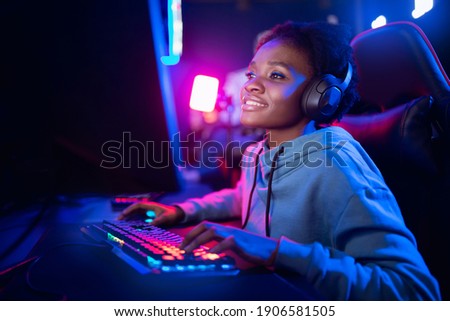 Professional Streamer African young woman cyber gamer studio room with personal computer armchair, keyboard in neon color blur background.