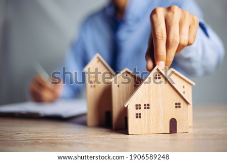 Businessman choosing mini wood house model from model on wood table, Planning to buy property. concept of Choose the best. Royalty-Free Stock Photo #1906589248