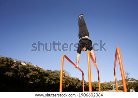 Low angle of a man doing handstand on the bar. Outdoor exercise. Concept of healthy living, sport, training, calisthenics.