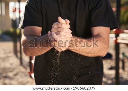 Close-up of a man's hands putting magnesium on his hands, preparing to do barbell exercises. With sand between his hands.