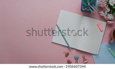 Top view of female blog writer workspace with notebook, stationery, pencils and copy space on pastel pink background.