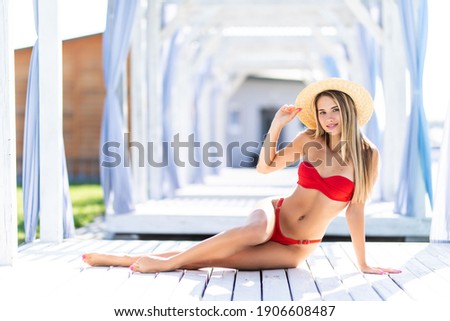 Young woman in swimsuit and straw hat relaxing on chaise-longue