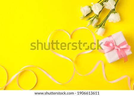 Gift box, heart made of ribbon and roses on yellow background