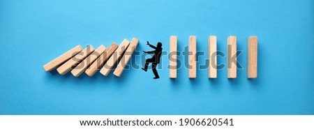 Silhouette of a man in panic against collapsing wooden dominos on blue background. Business crisis and failure concept in wide view.