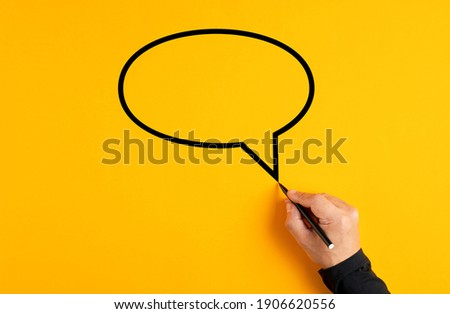 Male hand drawing a blank speech balloon on yellow background.