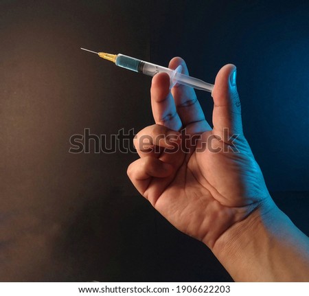 a hand holding a syringe with blue fluid inside it on dark background 