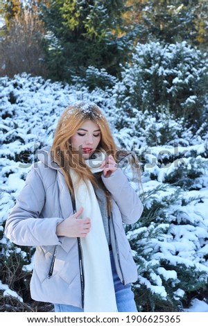 Snowy winter photos of a young blonde girl with fair skin in varishki scarf and gray jacket.

