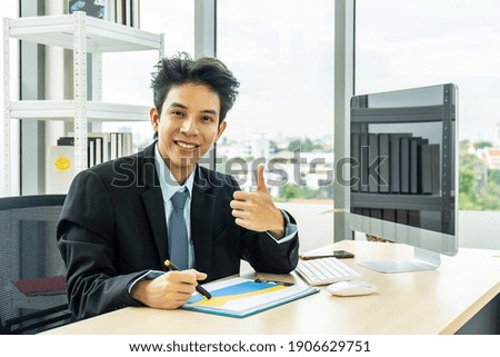 Successful confident asian businessman looking at camera,  showing thumbs up or like while using laptop in office, recommending best choice for business, sign of success, good idea, great job