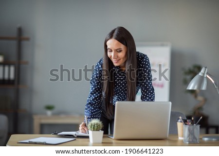 Photo of young business woman work in office write notebook computer indoors in workplace workstation