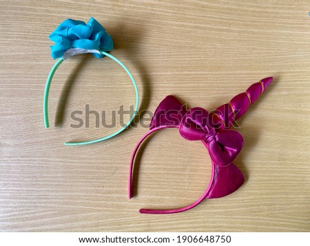 Two kid's headbands: a red-violet unicorn with a bow and a pretty blue turquoise ornament for the other. Cute accessories for little girl. Light brown wood texture background. Medium closeup.