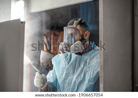 Painter in protective wear paints metal products with powder paint. Powder coating process at the manufacturing. High quality photo Royalty-Free Stock Photo #1906657054