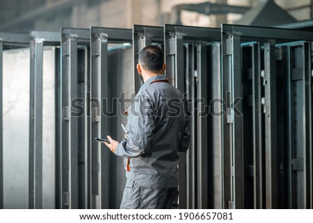 Engineer or factory worker in work wear using digital technology in the production of metal products, using a digital tablet at the plant. Rear view. High quality photo