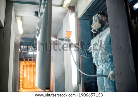 Painter in protective wear paints metal products with powder paint. Powder coating process at the manufacturing. High quality photo Royalty-Free Stock Photo #1906657153
