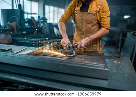 Metal industry worker dressed in apron doing some metalwork, grinding steel product at the factory. At the manufacturing of metal products. Close-up. High quality photo