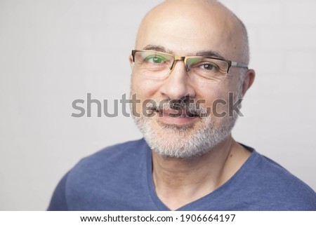 Portrait of a handsome positive 50 years old man with glasses, unshaven hair in a blue t-shirt indoors. Royalty-Free Stock Photo #1906664197