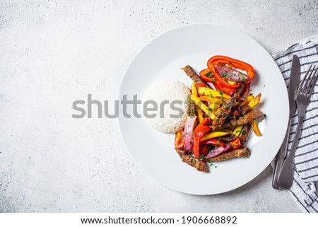 Peruvian cuisine concept. Lomo saltado - fried pieces of beef with peppers, onions and potatoes on a white plate. Royalty-Free Stock Photo #1906668892