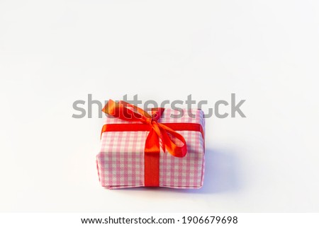 A box with a gift in a decorative white and pink package, Tied with a red ribbon. On a white background, a place to write.copy space