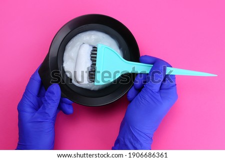 hairdresser holds a bowl of hair dye and a brush on a pink background Royalty-Free Stock Photo #1906686361