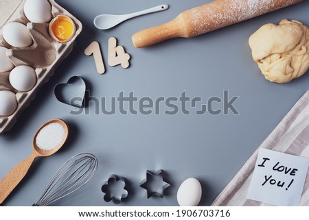 Making cookies for Valentine's Day, flat lay, top view, copy space. Various ingredients, rolling pin, dough, eggs, numbers 14, whisk on a gray background, layout on a gray background.