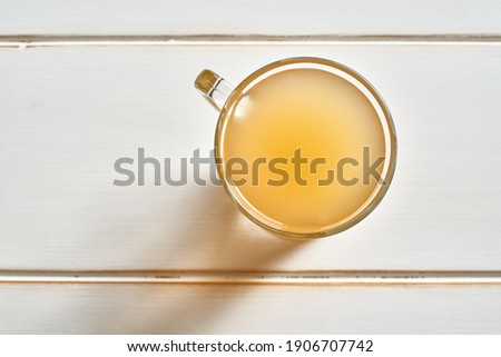 A cup of beef bone broth on a white wooden table, top view