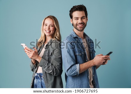 Young happy man and woman smiling and using mobile phones isolated over blue background