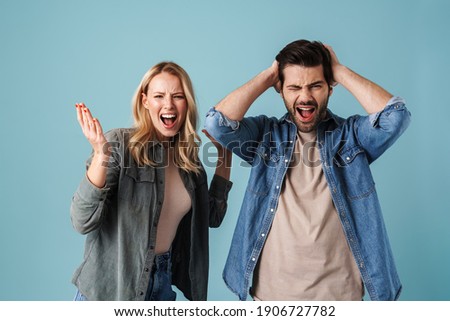 Young irritated man and woman screaming while having argument isolated over blue background