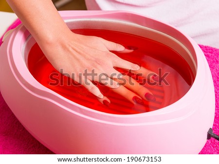 Female hand and orange paraffin wax in bowl. Manicure and skincare. Woman girl in beauty spa salon. Royalty-Free Stock Photo #190673153