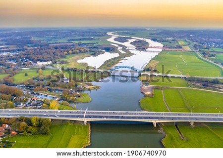 Aerial view of huge lowland river IJssel with highway and railroad bridges through sunset landscape. Zwolle, Overijssel Province, the Netherlands. Drone scene in nature of Europe. Royalty-Free Stock Photo #1906740970