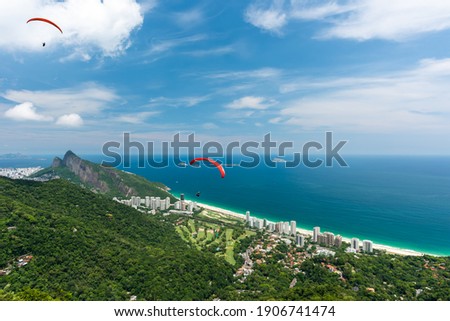Beautiful scenery from above of free flight ramp overlooking the São Conrado beach, emerald sea, lush vegetation with a hang glider over the sky of Rio de Janeiro. Royalty-Free Stock Photo #1906741474