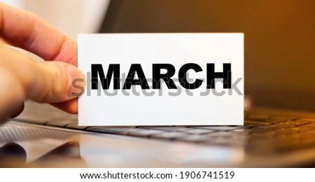 A man holding a white business card with the word - March