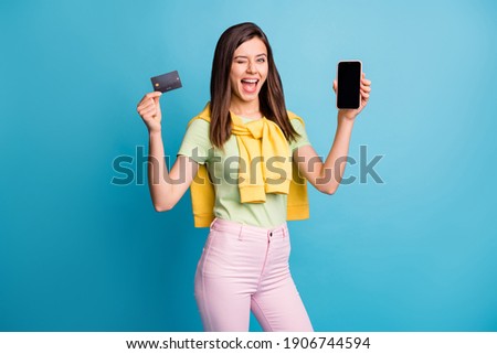 Photo of young beautiful crazy excited smiling woman girl wink eye show credit card phone isolated on blue color background