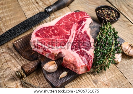 Raw Porterhouse or T-bone beef meat Steak with herbs on a wooden cutting board. wooden background. Top view Royalty-Free Stock Photo #1906751875