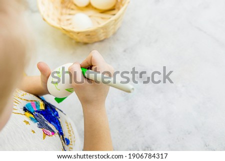 children's hands draw an Easter bunny on a white egg with a marker pen on the background of an egg basket and a gray marble background