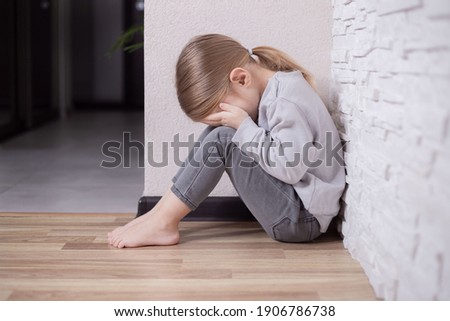 Sad little child girl sitting on floor in corner at home. Royalty-Free Stock Photo #1906786738