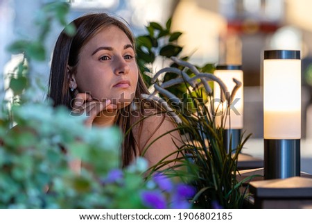  young beautiful woman sitting at table of street cafe and waiting for meeting, defocused flowers in the foreground